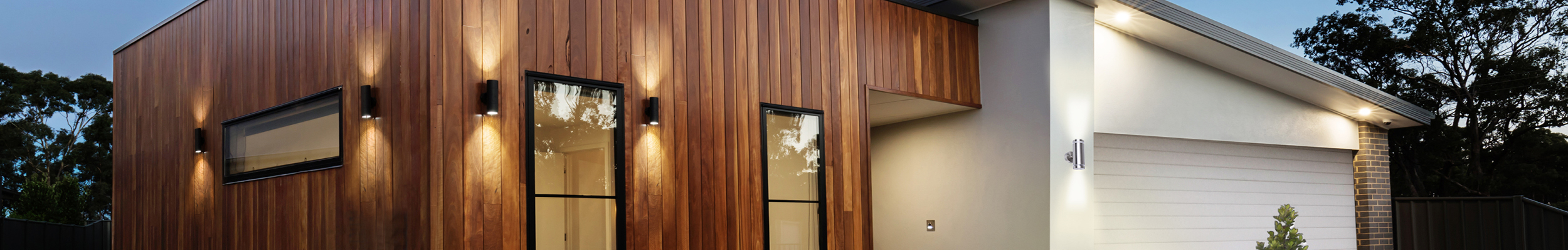 Modern house clad in wood with Integral LED Stainless Steel Outdoor Up & Down Wall lights on the exterior walls in both black and steel colourways