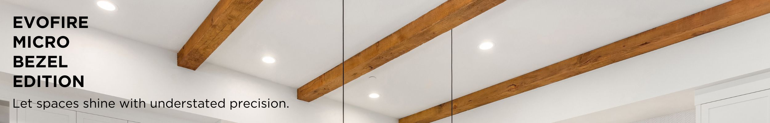 Modern white kitchen. Image focus on ceiling with wood beams and downlights. Text reads 'Evofire Micro Bezel Edition. Let spaces shine with understated precision.' 